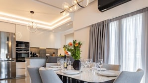 A modern dining area with a round table, grey upholstered chairs, and a vase of flowers. - Parthenon View Luxury Penthouse (Athens)