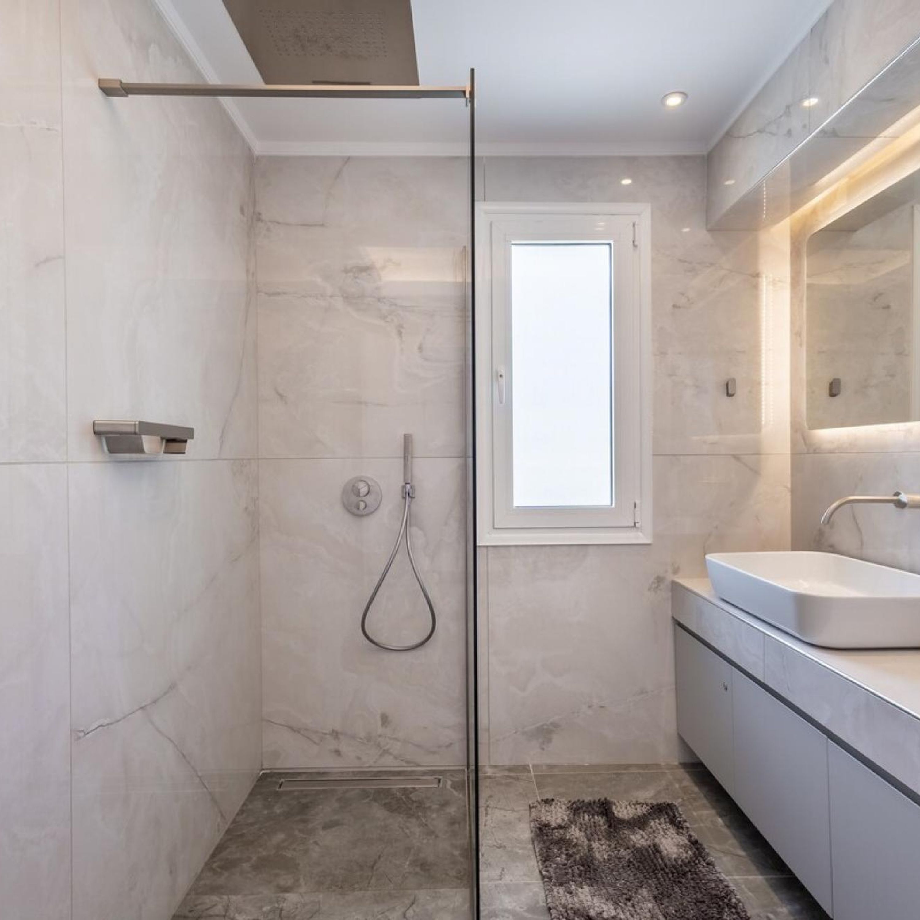 A modern bathroom with a glass shower enclosure, a large mirror, and a white sink.