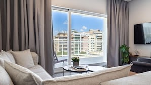 A modern living room with a large window, a sofa, a coffee table, and a TV. - Parthenon View Luxury Penthouse (Athens)