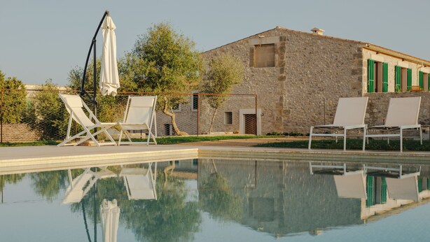 Ein Swimmingpool mit Liegestühlen und einem Sonnenschirm, umgeben von einem Steinhaus mit grünen Fensterläden.
