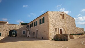 Ein Steinhaus mit großem Bogenportal und einer Treppe, die zu einer oberen Ebene führt, unter blauem Himmel.