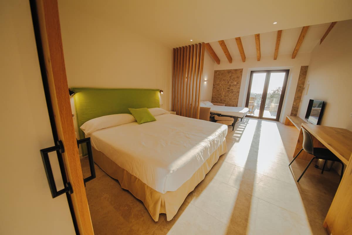 A bedroom with a large bed, a desk, and a view of the outdoors.