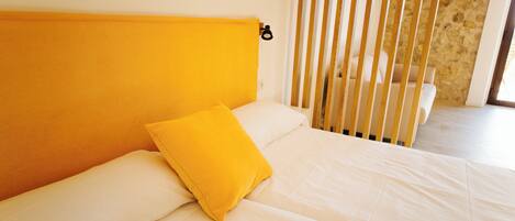 A bed with white bedding and a single yellow pillow, a wooden headboard, and a stone wall in the background.