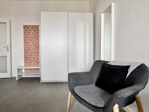 A room with a grey armchair, a white wardrobe, and a patterned curtain.