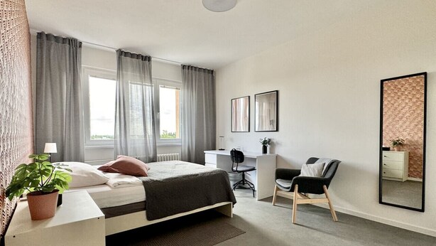 Moderni hotellihuone, jossa on sänky, työpöytä, tuoli ja suuri peili.