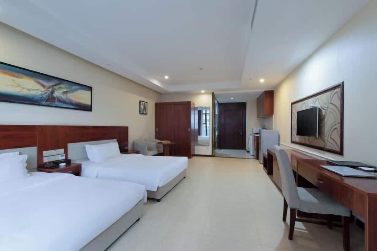 Ein Hotelzimmer mit zwei Betten, einem Schreibtisch, einem Stuhl, einem Fernseher und Bildern an den Wänden.