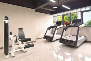 A gym with treadmills and weight machines, large windows with a view of greenery, and a polished floor. - Mujinhua Hotel (Chongqing)