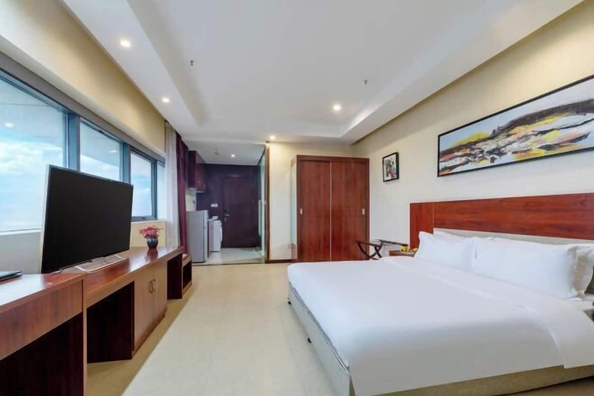 Ein Hotelzimmer mit einem großen Bett, einem Fernseher auf einer Holzkonsole, einem Bild an der Wand und Blick durch ein Fenster.