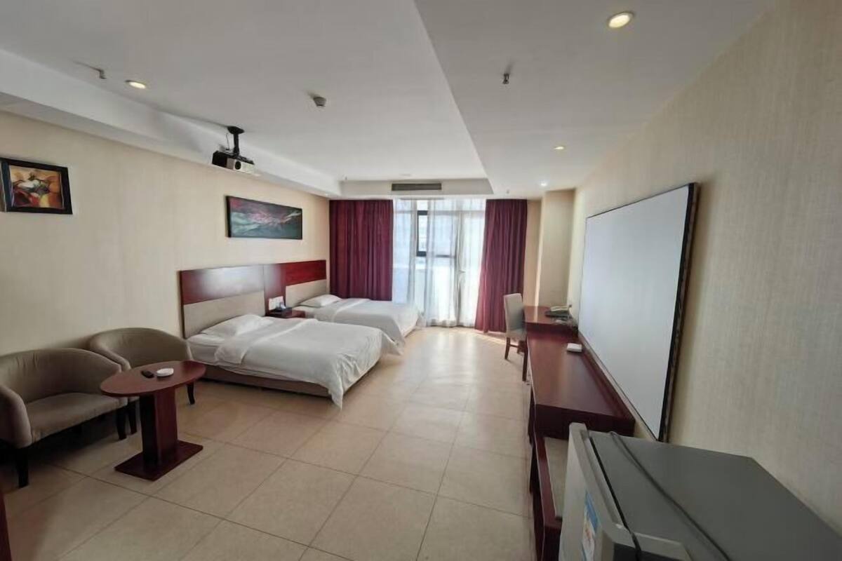 Ein Hotelzimmer mit zwei Betten, einer Schlafcouch, einem Schreibtisch und einem Flachbildfernseher.