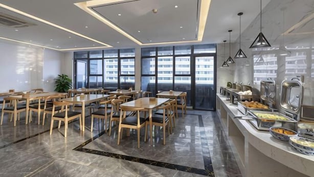 Un espace repas moderne avec des tables et des chaises en bois, un buffet proposant différents plats, et de grandes fenêtres laissant entrer la lumière naturelle.
