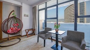 Une pièce dotée d’une grande fenêtre, d’un fauteuil suspendu, de deux fauteuils, d’une petite table et offrant une vue sur un bâtiment situé de l’autre côté de l’eau.