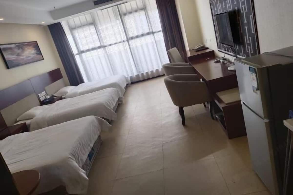 Ein Hotelzimmer mit zwei Betten, einem Schreibtisch mit Stuhl, einem Fernseher und einem Kühlschrank.