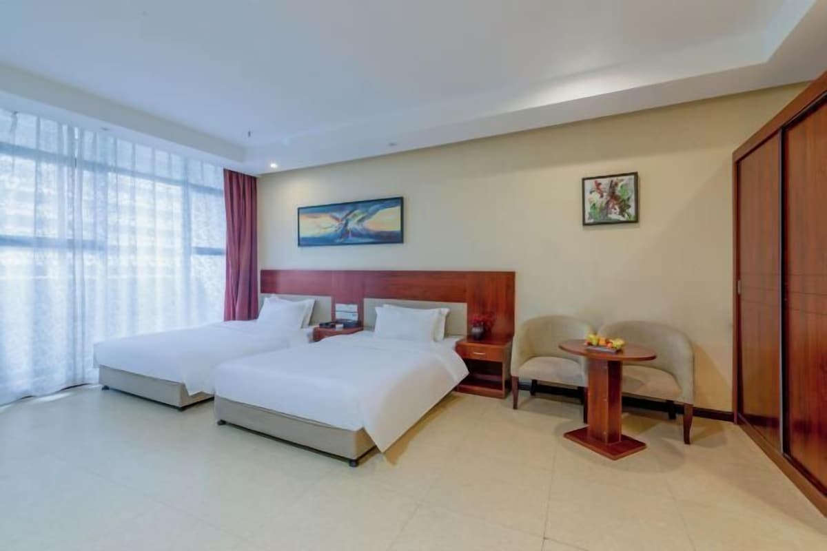 A hotel room with two beds, a wooden headboard, a small table with fruit, and a chair.
