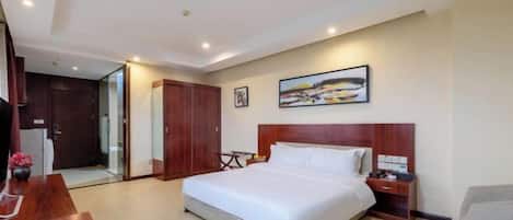 A hotel room with a large bed, a wooden headboard, a bedside table, a chair, a desk, and a painting on the wall.