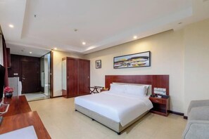A hotel room with a large bed, a wooden headboard, a bedside table, a chair, a desk, and a painting on the wall. - Mujinhua Hotel (Chongqing)