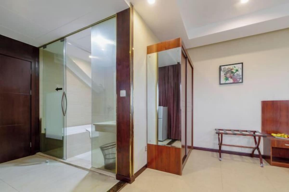 A room with a sliding glass door leading to a shower area, a wooden wardrobe, a mirror, and a small table with a chair.