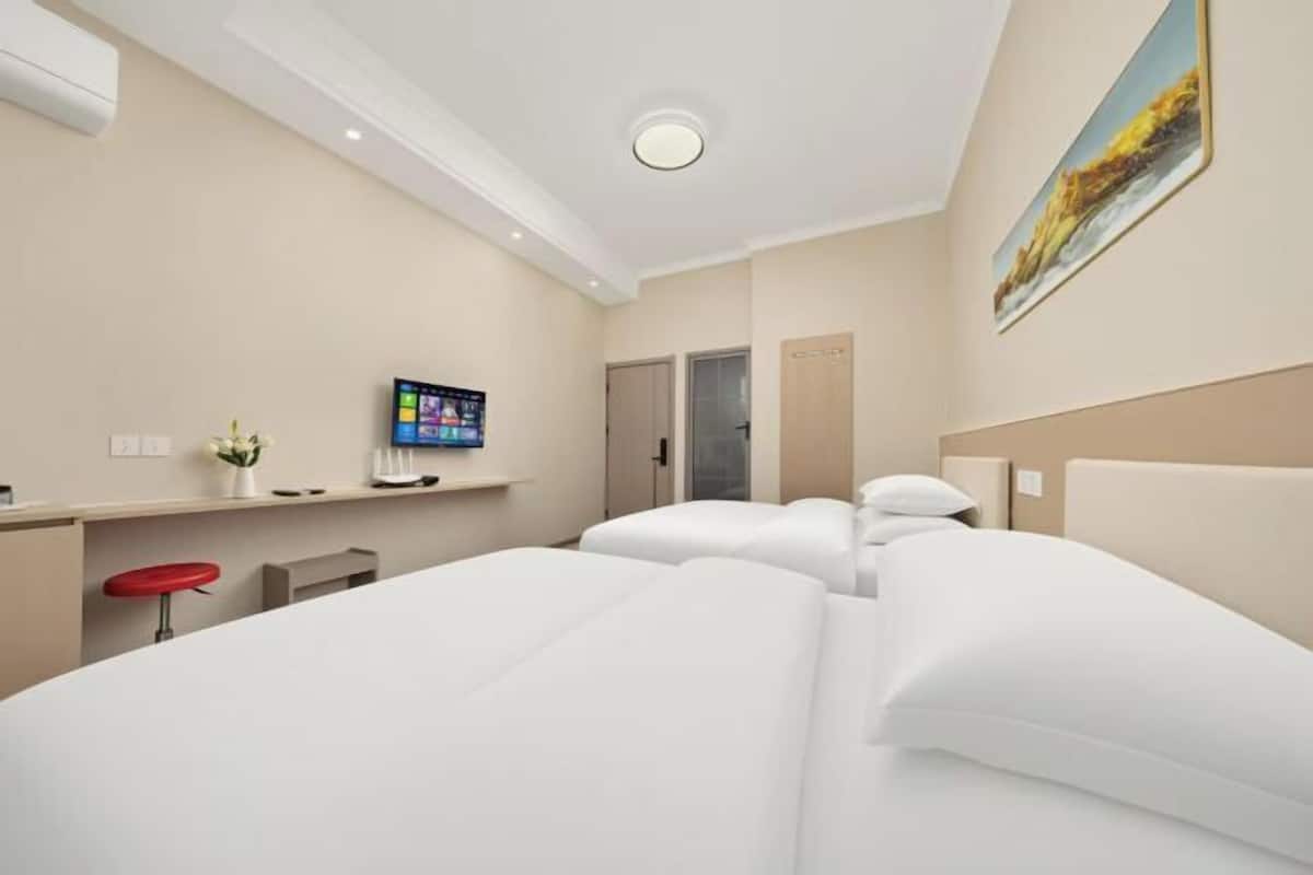 A hotel room with a bed, a desk, a TV, and a painting on the wall.