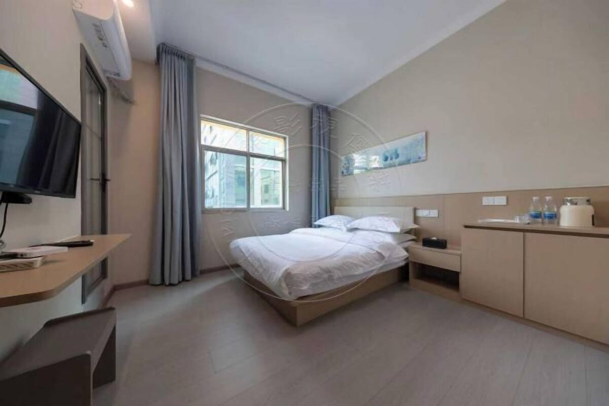 A hotel room with a bed, a desk, a TV, a window with curtains, and a painting on the wall.