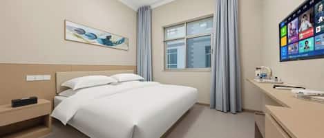A hotel room with a bed, bedside table, a desk with a chair, a window with curtains, and a wall-mounted TV.