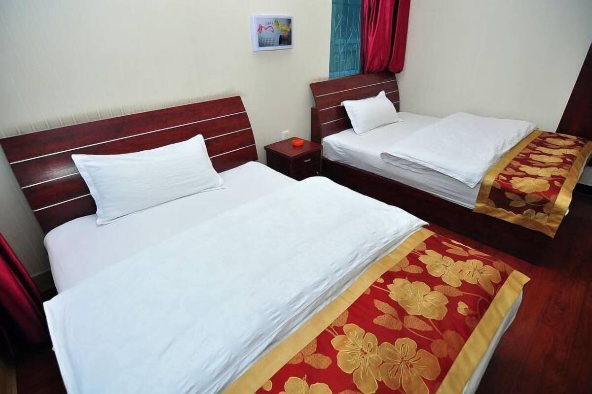 Two beds with wooden headboards, white bedding, and a red floral bedspread.