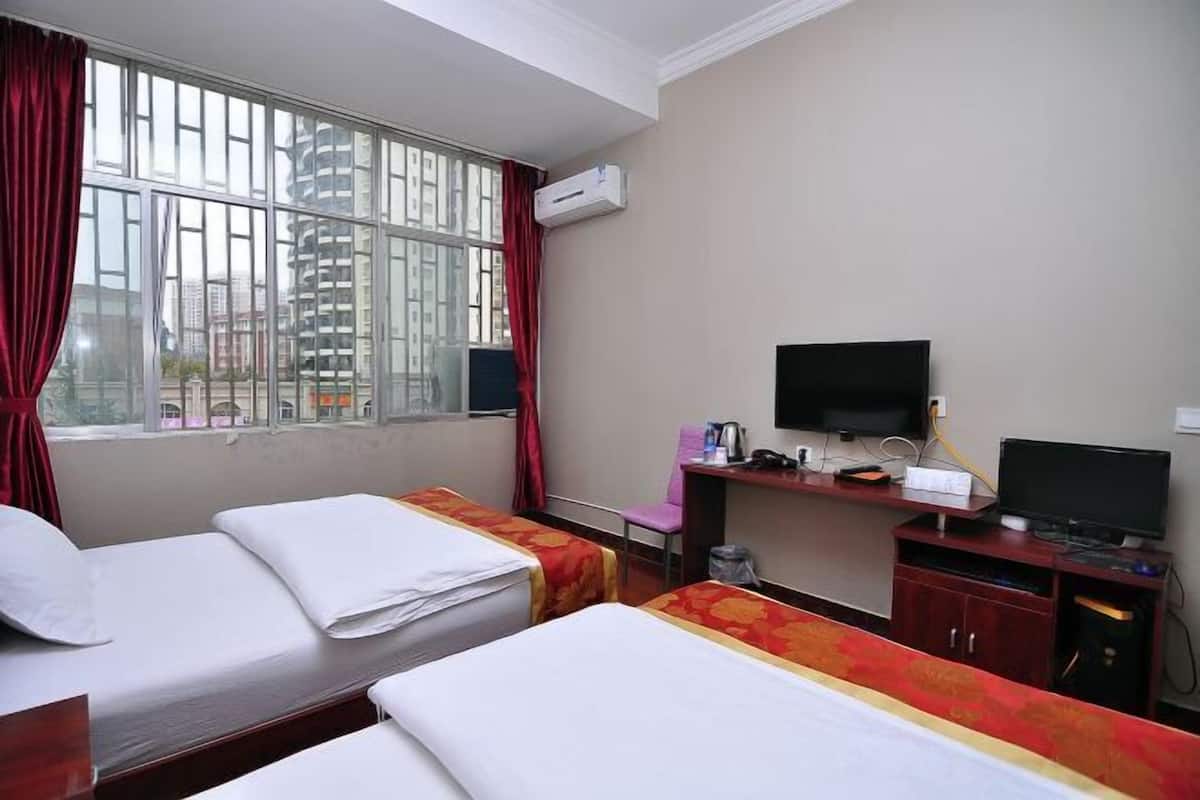 A hotel room with two beds, a desk with a television, and a window with a view of buildings.