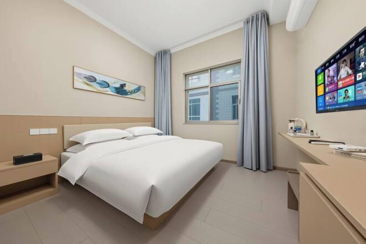 A hotel room with a bed, a desk, a television, and a window with curtains.