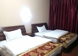 A hotel room with two beds, a nightstand, and a red curtain.