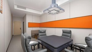 A conference room with a rectangular table, four grey chairs, a sofa, and a large orange accent wall. - Vienna Hotel Haikou International Trade City Friendship Sunshine City (Haikou)
