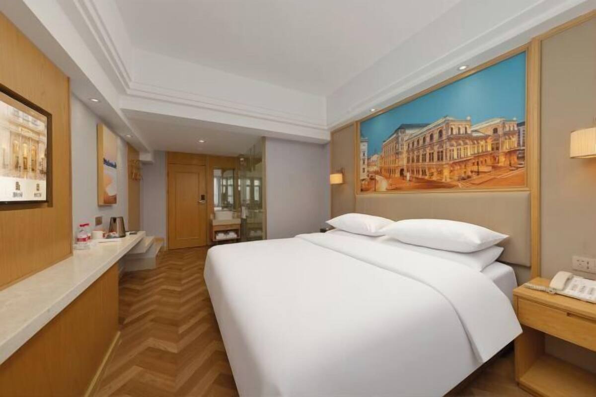 Ein Hotelzimmer mit einem Bett, einem Nachttisch, einem Gemälde und Holzboden.