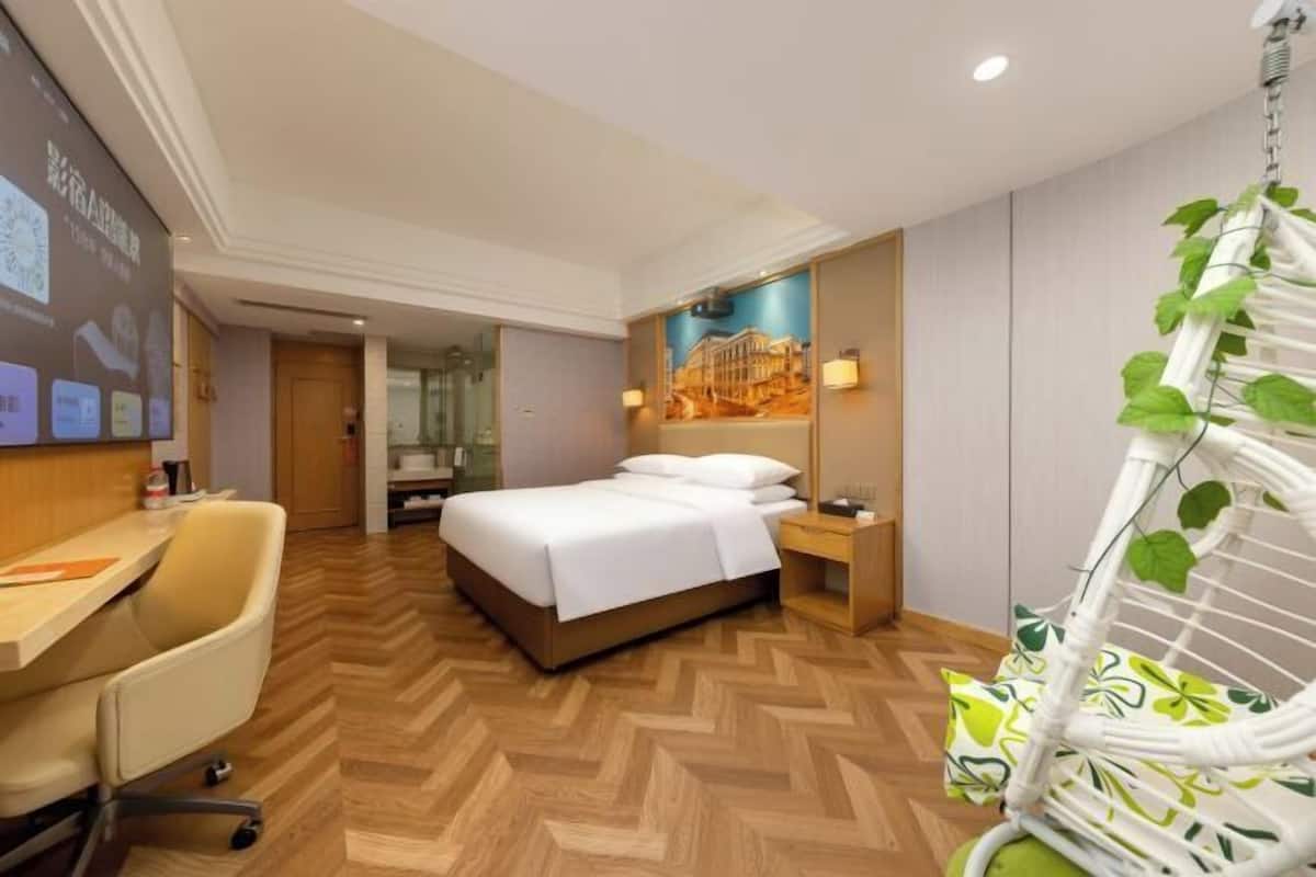 Ein Hotelzimmer mit Bett, Schreibtisch, Stuhl, Hängesessel und einem Wandbild.