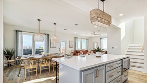 A spacious kitchen with a large island, wooden dining table, and pendant lighting. - Surfside Beachfront Paradise (Surfside Beach)
