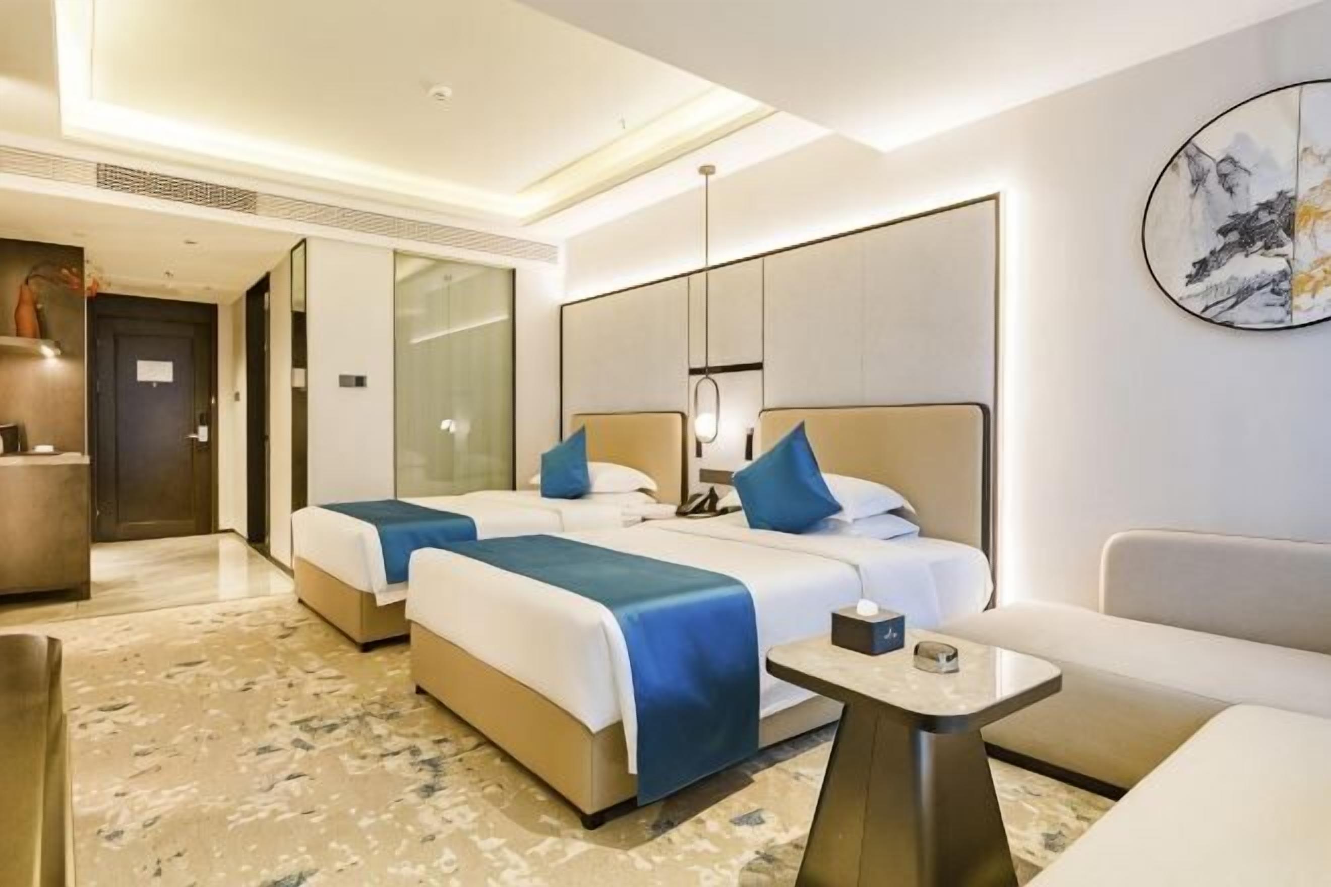 A hotel room with two beds, a sofa, a small table, and a large window.