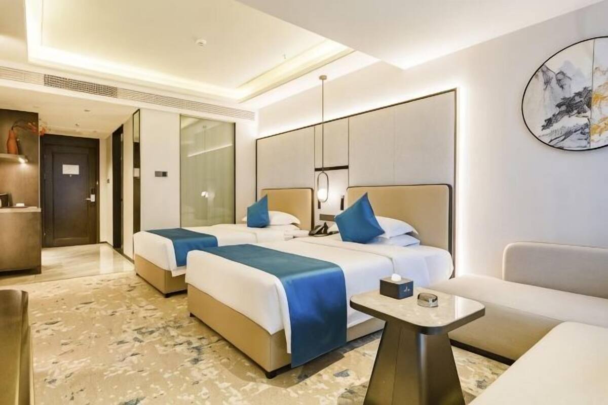 A hotel room with two beds, a sofa, a small table, and a large window.