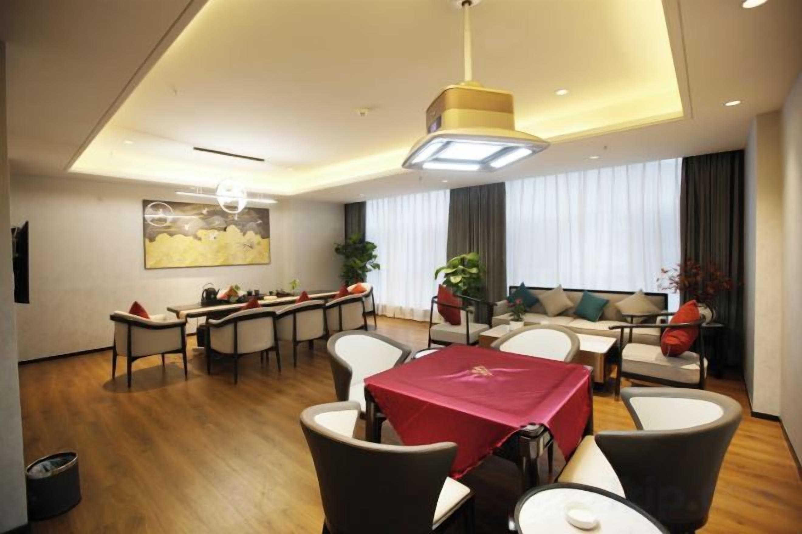 A modern hotel room with a dining area, a sofa set, and a large window with curtains.