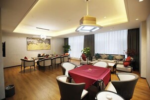 Una habitación de hotel moderna con zona de comedor, un conjunto de sofás y un amplio ventanal con cortinas.