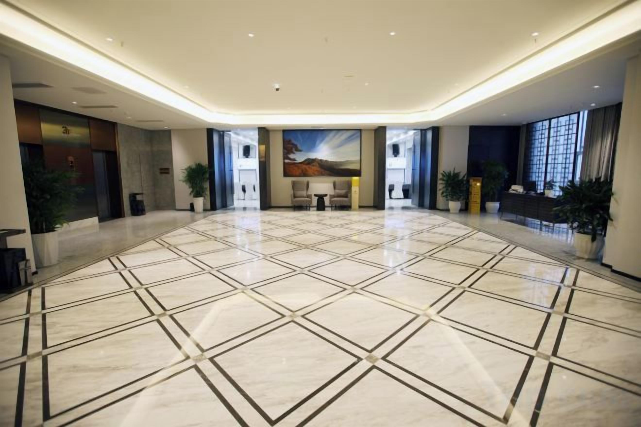 A spacious lobby with a tiled floor, a reception desk, and potted plants.