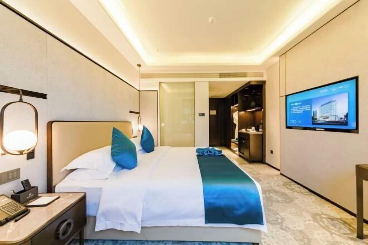 A hotel room with a bed, bedside table, and a TV mounted on the wall.