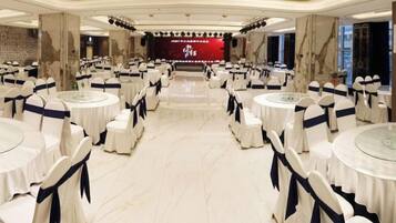 A banquet hall with round tables and chairs, a stage with a red backdrop, and marble flooring.