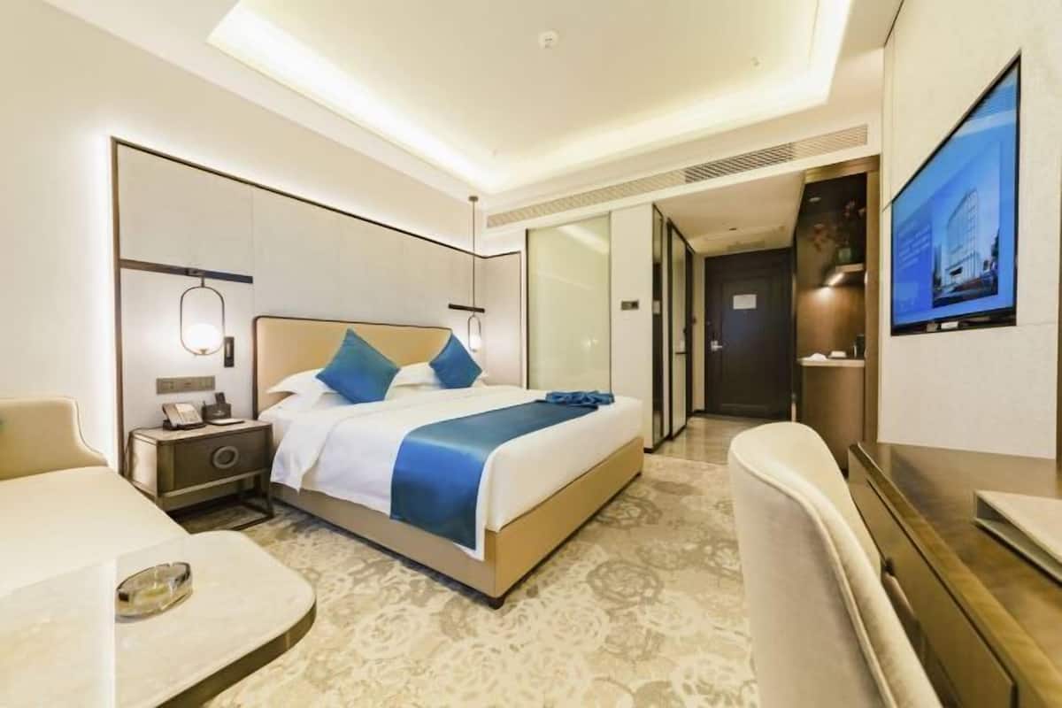A modern hotel room with a bed, bedside table, lamp, TV, and a seating area.