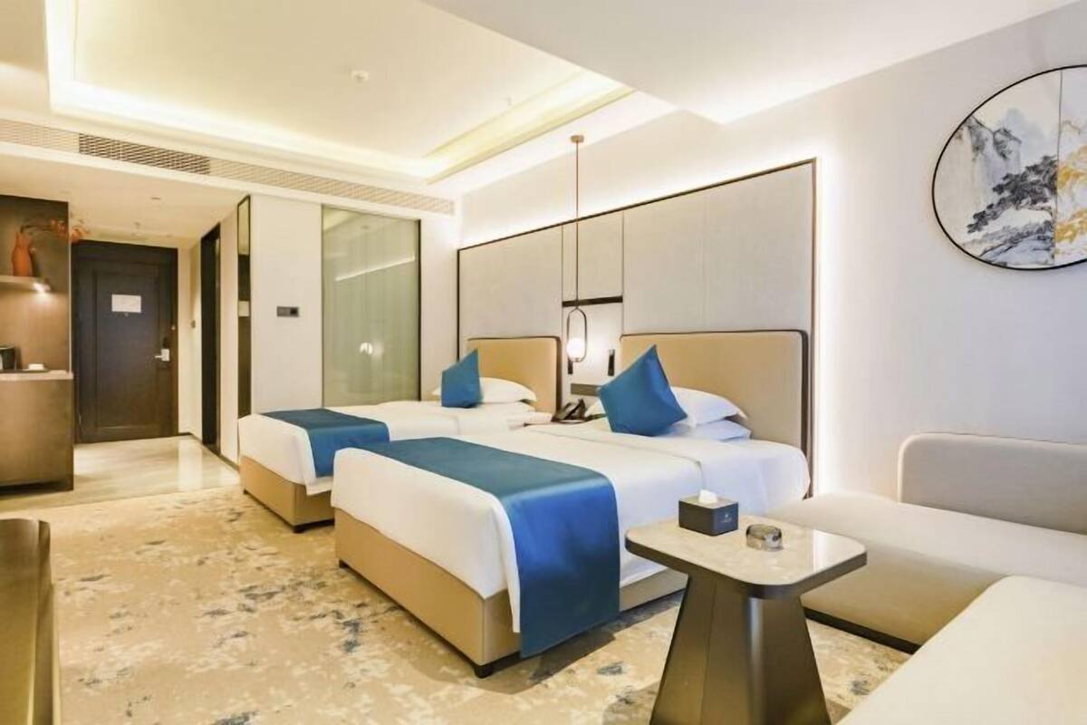 A hotel room with two beds, a small table, a sofa, and a painting on the wall.
