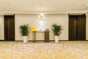 Un área de recepción con mostrador, dos plantas en macetas y piso alfombrado.