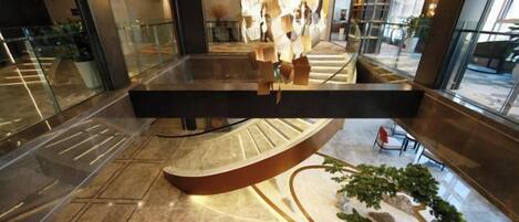 Un vestíbulo moderno con una escalera central, un área de descanso y un arreglo decorativo de plantas.