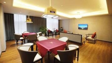 Une salle à manger d’hôtel avec une table rouge, des chaises blanches, un bar et un tableau accroché au mur.