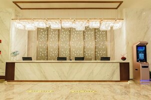 Una zona de recepción con mostrador de mármol, un panel decorativo grande y un quiosco digital de información.
