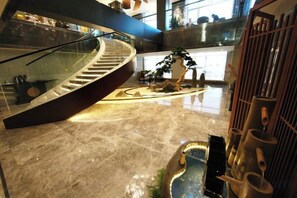 Un interior moderno con una escalera de cristal curva, una isla central con una escultura de árbol y un perchero metálico con objetos cilíndricos.