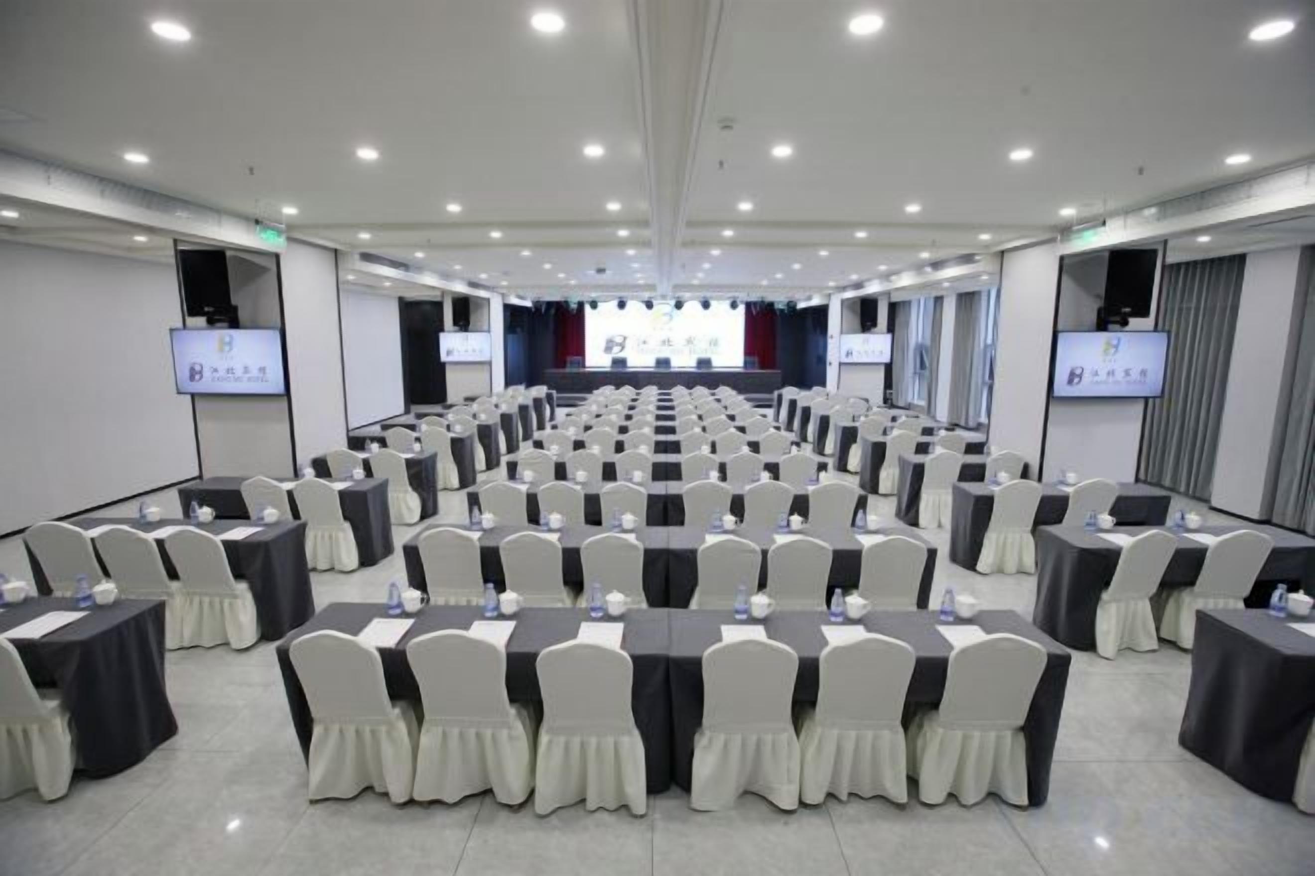A conference room with rows of tables and chairs, equipped with projectors and screens.