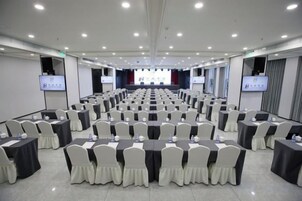 Un salón de conferencias con filas de mesas y sillas, equipado con proyectores y pantallas.