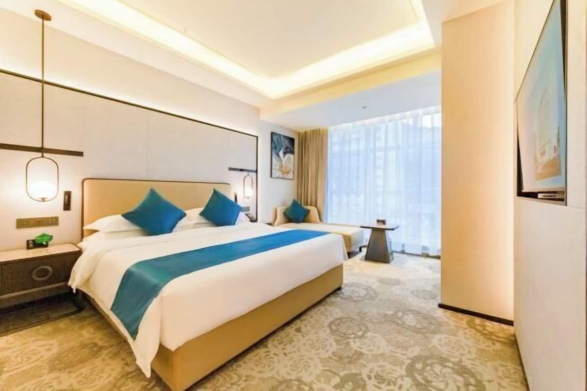 A hotel room with a large bed, bedside tables, a small table, and a large window with curtains.