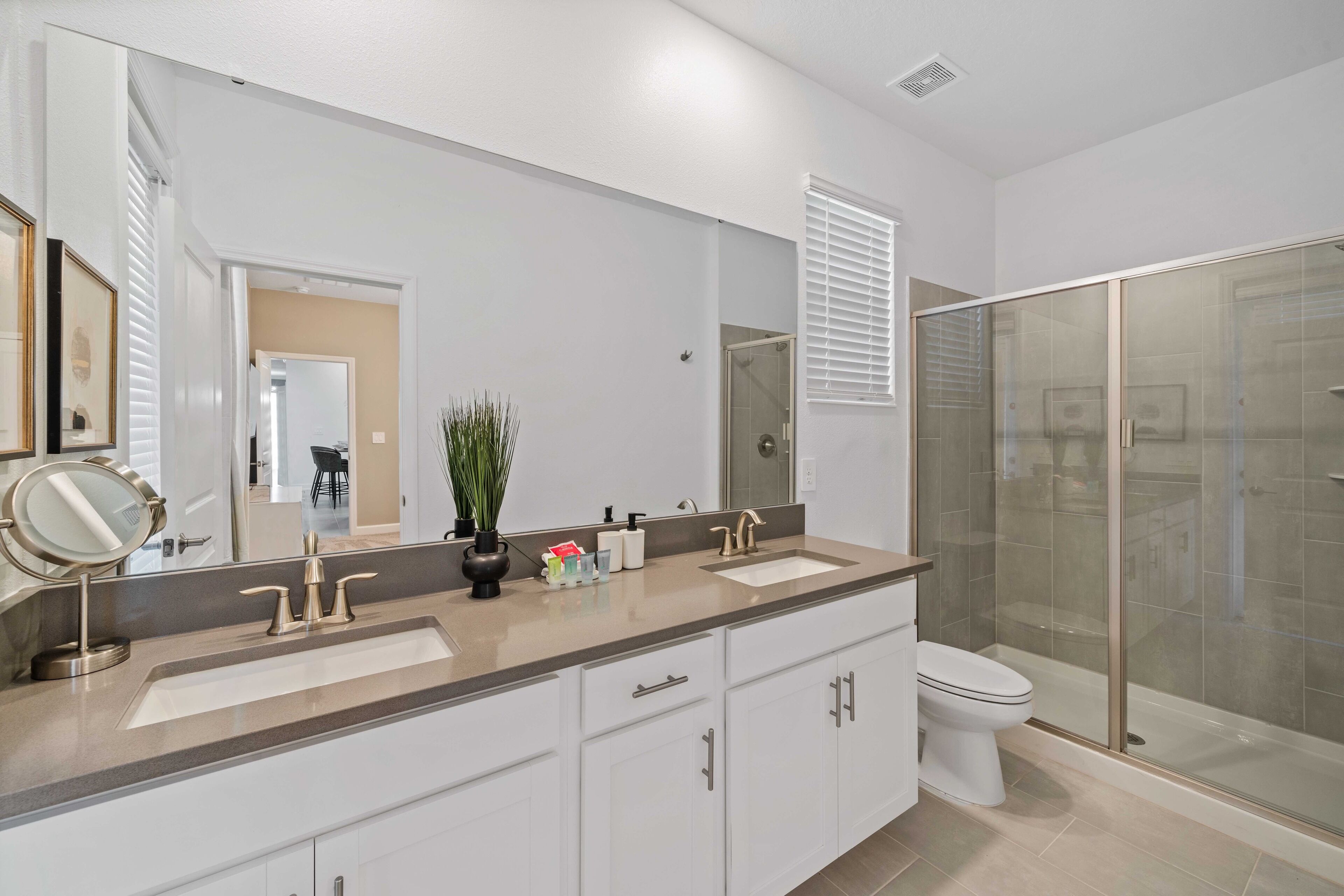 A modern bathroom with a large mirror, two sinks, a toilet, and a glass-enclosed shower.