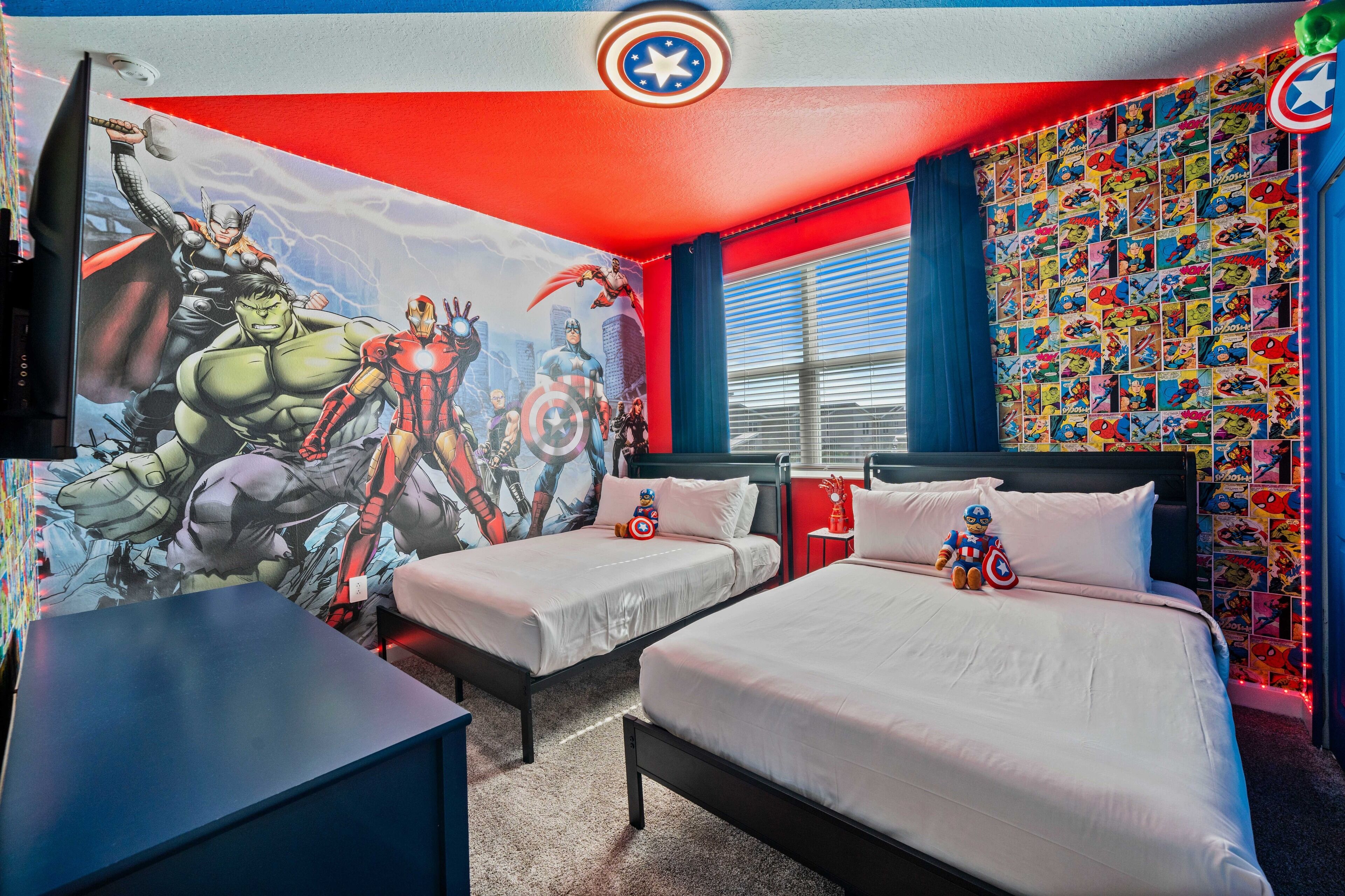 A bedroom with two beds, a mural on the wall, and a wall of comic book posters.
